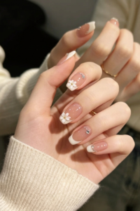 Glossy pink French manicure nails with small flowers at the tips.