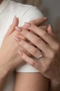 Elegant and youthful nude pink almond-shaped nails with polka dots.