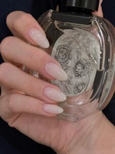 A hand with almond-shaped nails is holding a sophisticated and elegant perfume bottle.