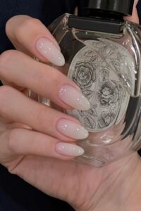 A hand with almond-shaped nails is holding a sophisticated and elegant perfume bottle.