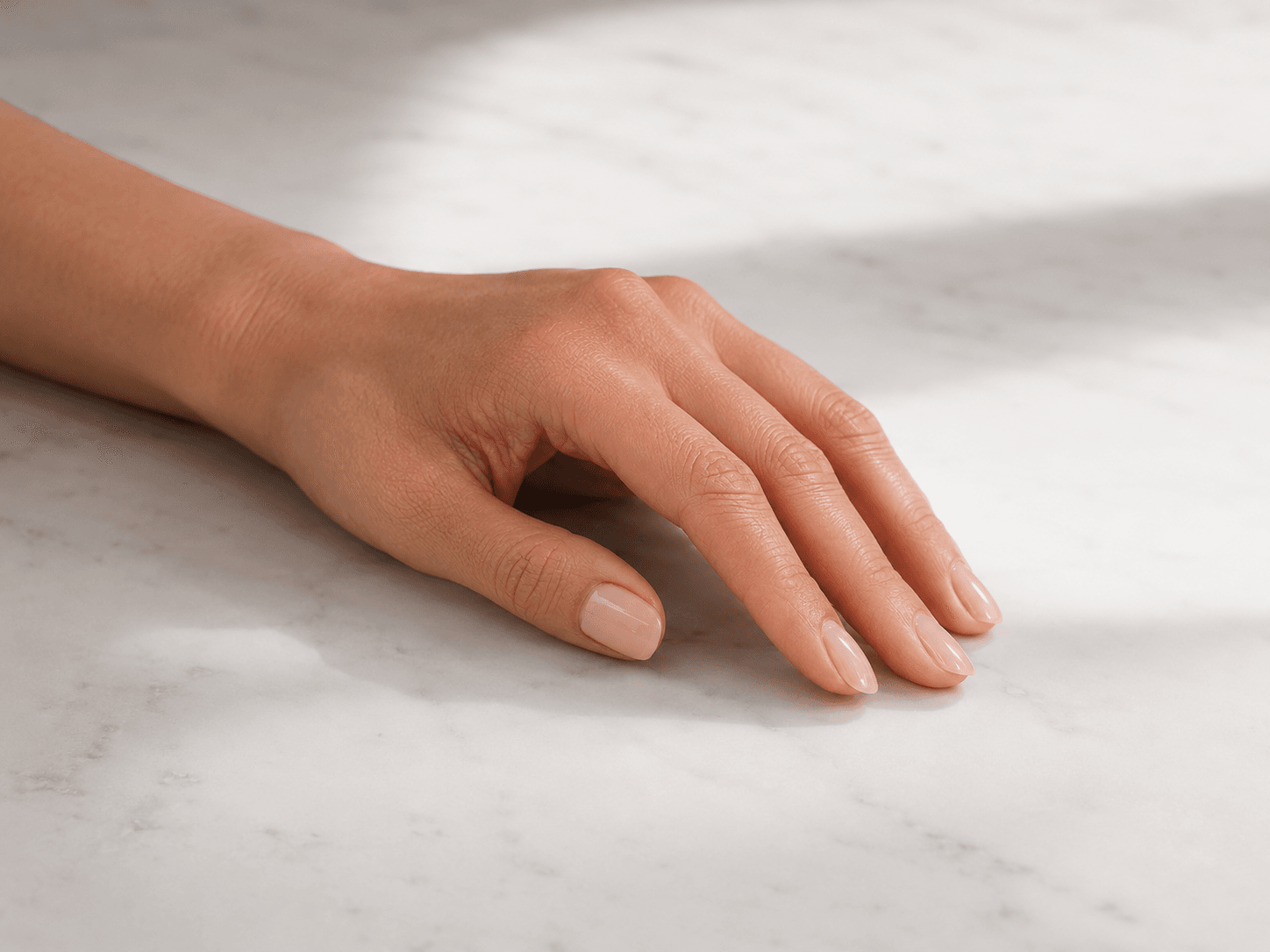 A minimalist hand pose on a white marble background with natural light, showcasing the pure elegance of a clean and timeless manicure.