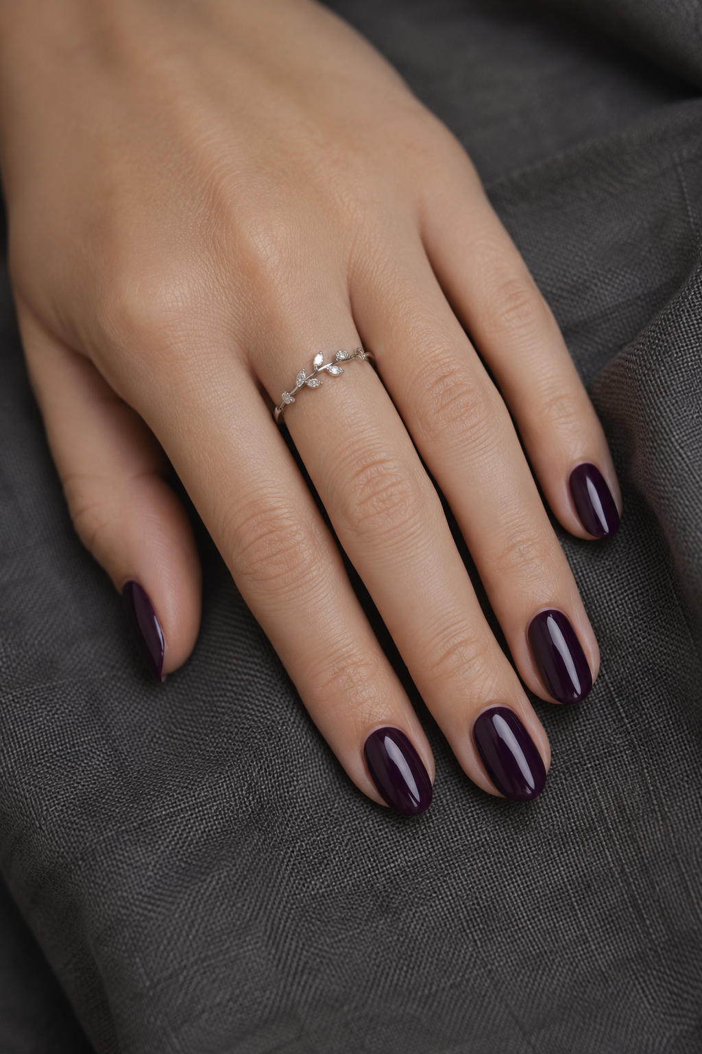 Deep plum nails with a jewel-toned smoky amethyst finish on oval-shaped nails, soft studio light.