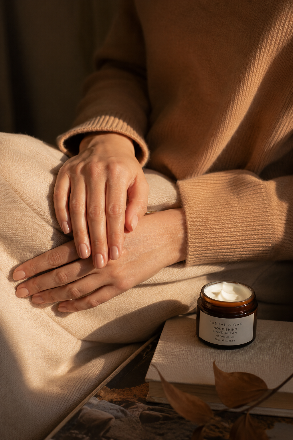 Softly lit feminine hands with healthy nails and moisturized skin in a cozy autumn setting, reflecting a consistent fall hand care routine.