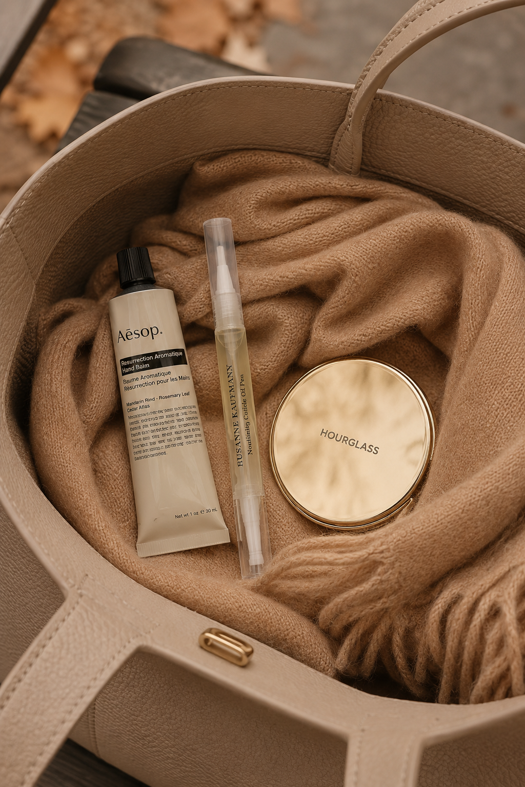 Travel-size hand cream and cuticle oil pen tucked into a leather tote bag for an on-the-go fall hand care routine.