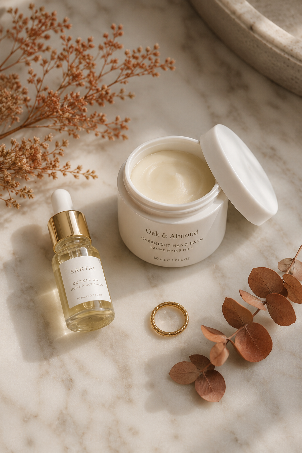 Quiet luxury flatlay of fall hand care products including cuticle oil and overnight hand balm on marble.