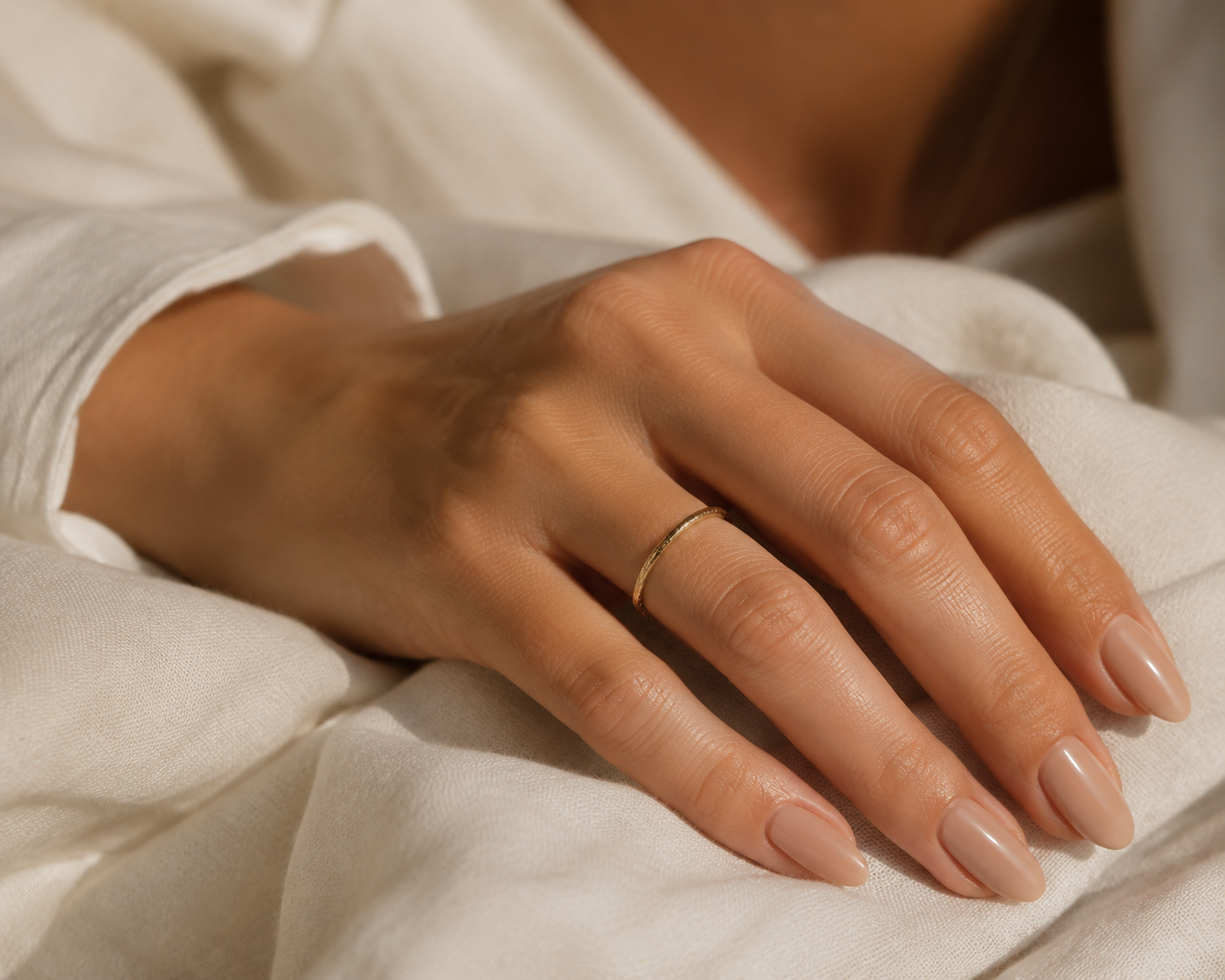Glossy nude monochrome manicure on almond-shaped nails resting on linen, quiet luxury nail aesthetic.