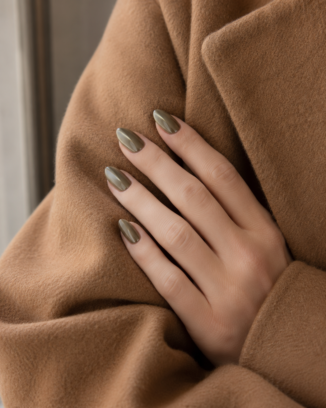 Muted olive chrome manicure styled against a camel wool coat for fall 2026