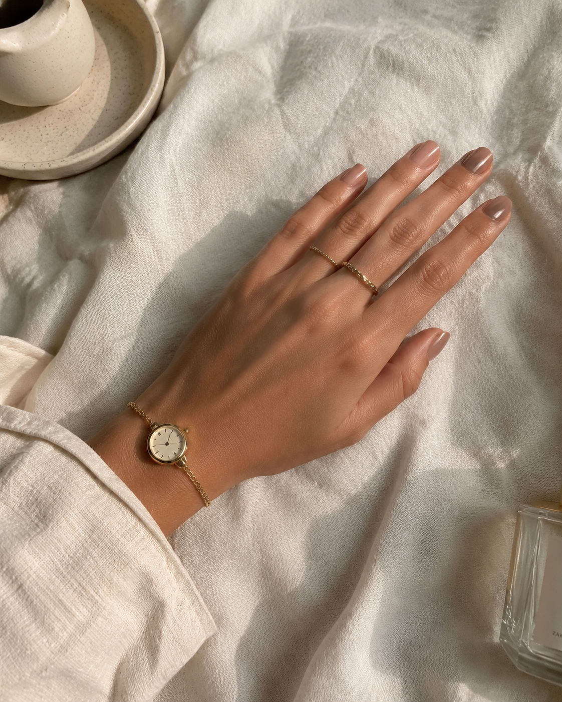 Woman's hand with a glossy nude manicure styled with minimal gold rings and a delicate watch